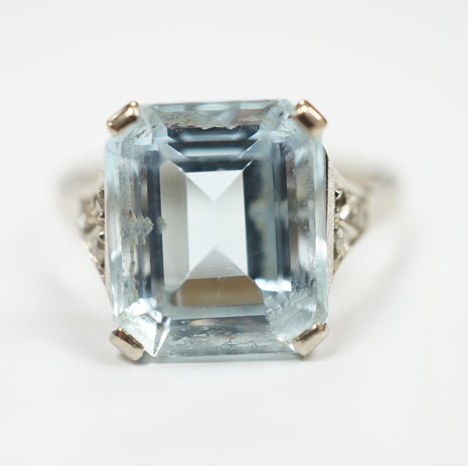 A white metal and single stone emerald cut aquamarine set ring, with rose cut diamond chip set shoulders (one stone missing), size M, gross weight 3.2 grams.